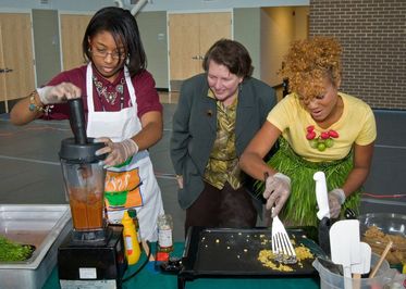 2 black women doing cooking demonstration with onlooker